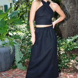 Woman wearing a black halter top and skirt standing outdoors with greenery in the background