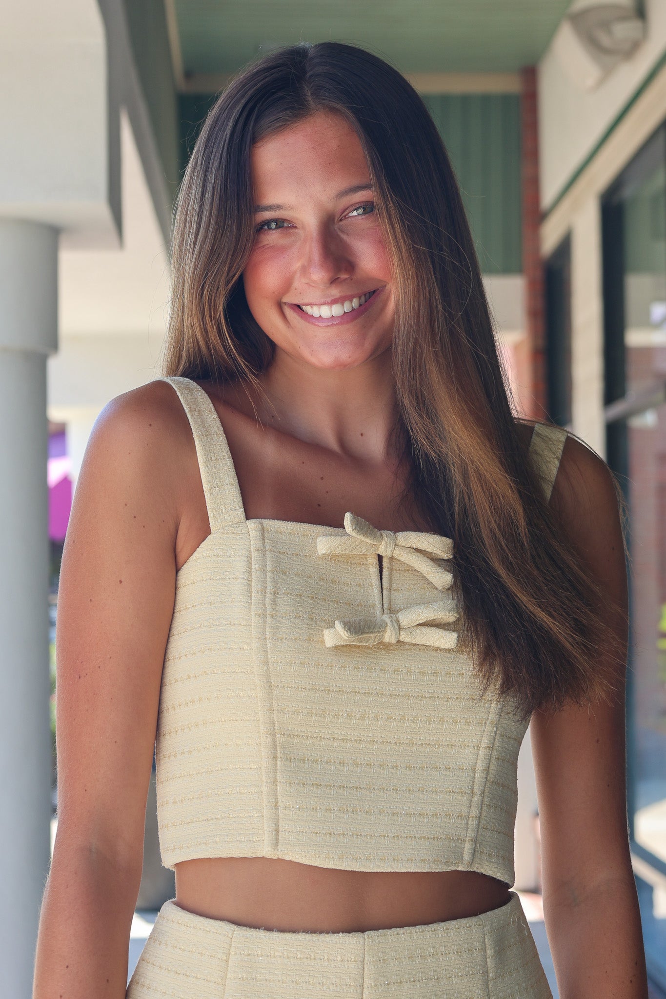 Woman wearing a light-colored top with straps and a skirt, standing outdoors.