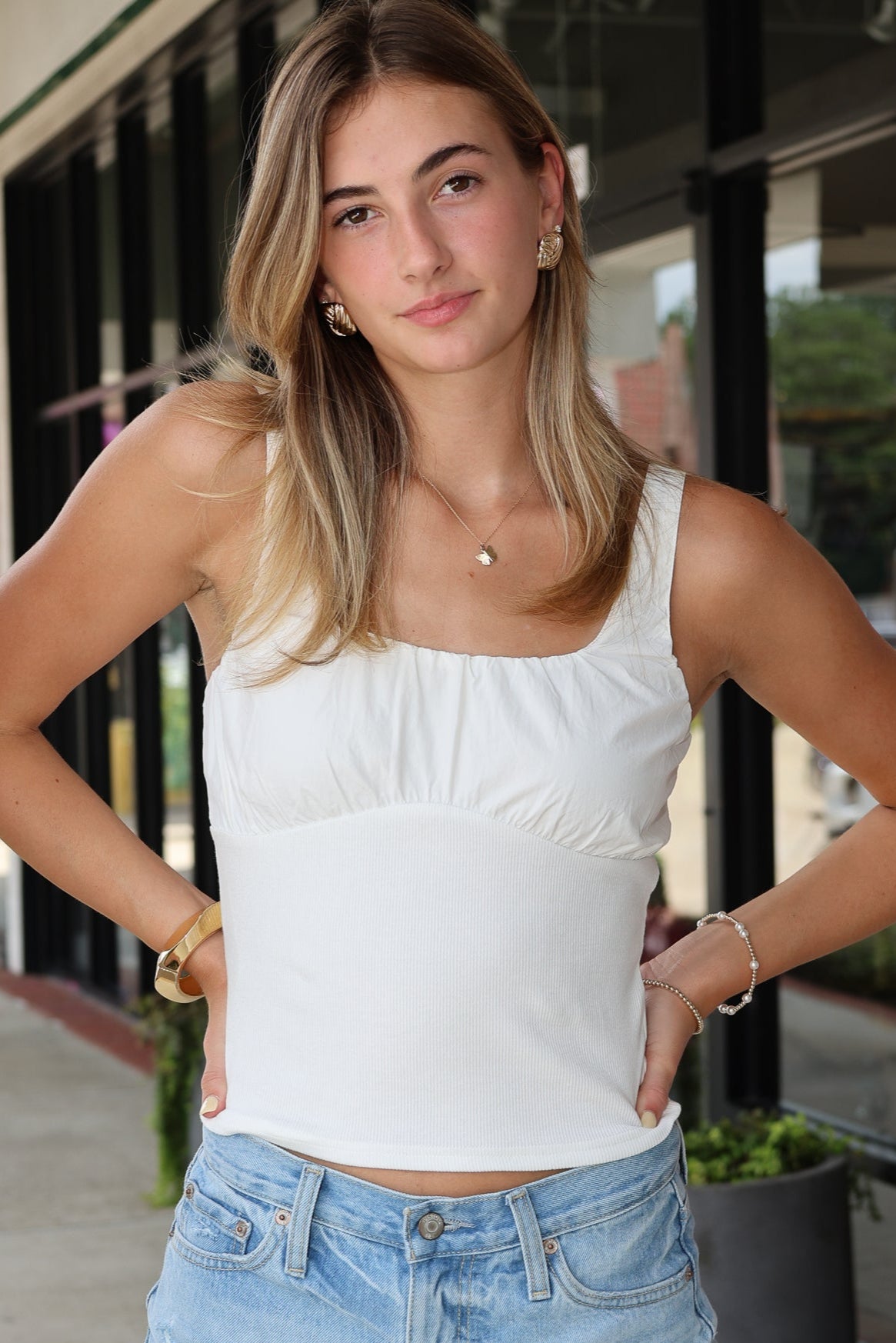 Woman wearing a white tank top and denim shorts standing outdoors.