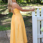 Woman in a strapless dress standing outdoors near a white picket fence.