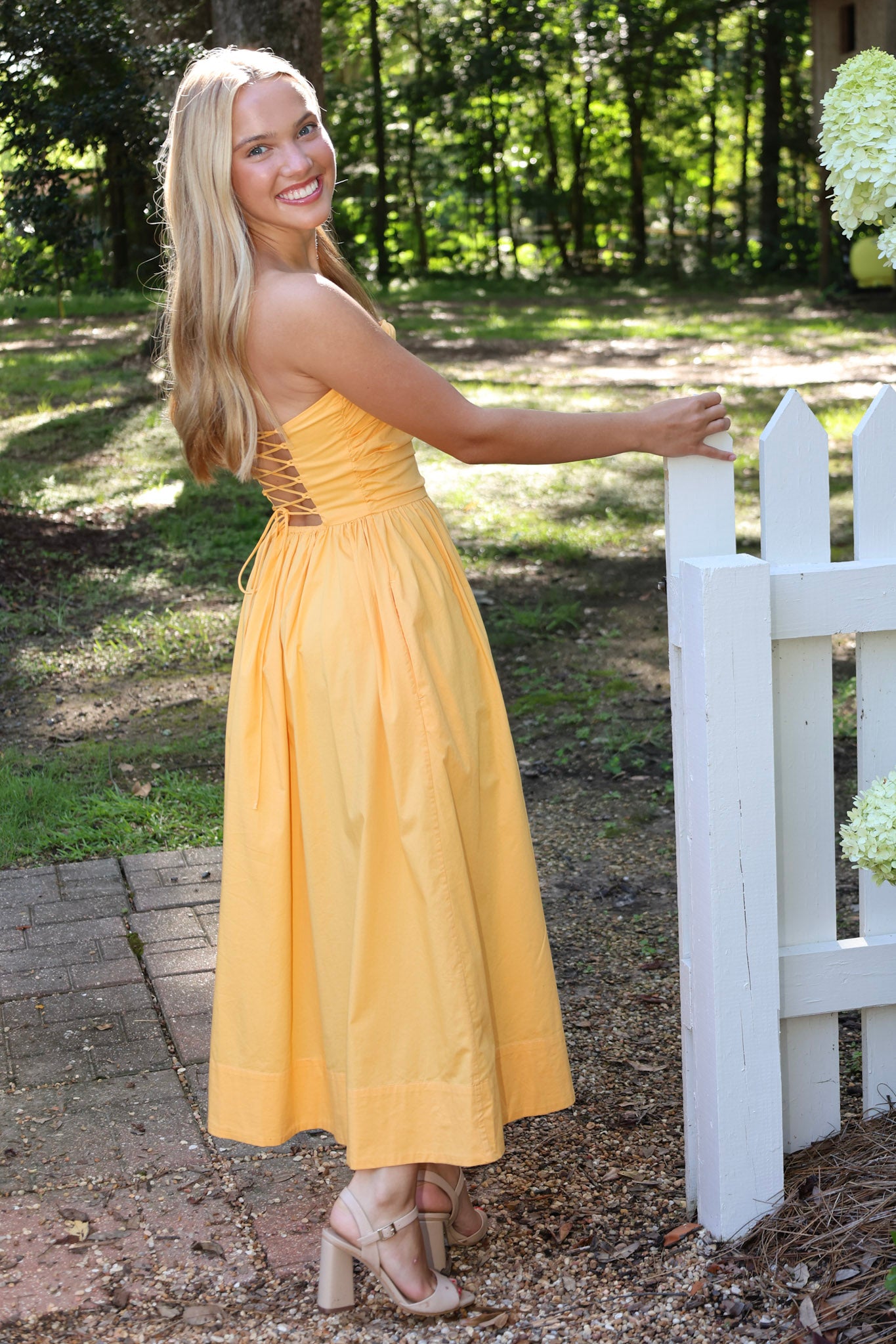 Woman in a strapless dress standing outdoors near a white picket fence.