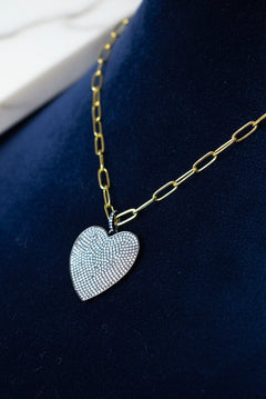 A gold-colored chain necklace with a black and silver oversized heart-shaped pendant on a mannequin bust.