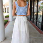 Woman wearing a blue ruffled top and white skirt walking outdoors.