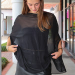 A woman wearing a sheer black mesh poncho-style top over a black faux-leather mini skirt, standing on an outdoor walkway.