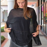 A woman wearing a sheer black mesh poncho-style top over a black faux-leather mini skirt, standing on an outdoor walkway.