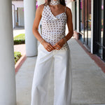 Woman wearing a polka dot top and white pants standing on a sidewalk.