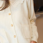 A close-up of a person wearing a cream-colored knit cardigan with a large white lace Peter Pan collar and light wood buttons, paired with a denim skirt at Rodeo Boutique..