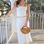 Woman in a white outfit holding a wooden handbag on a wooden deck on vacation