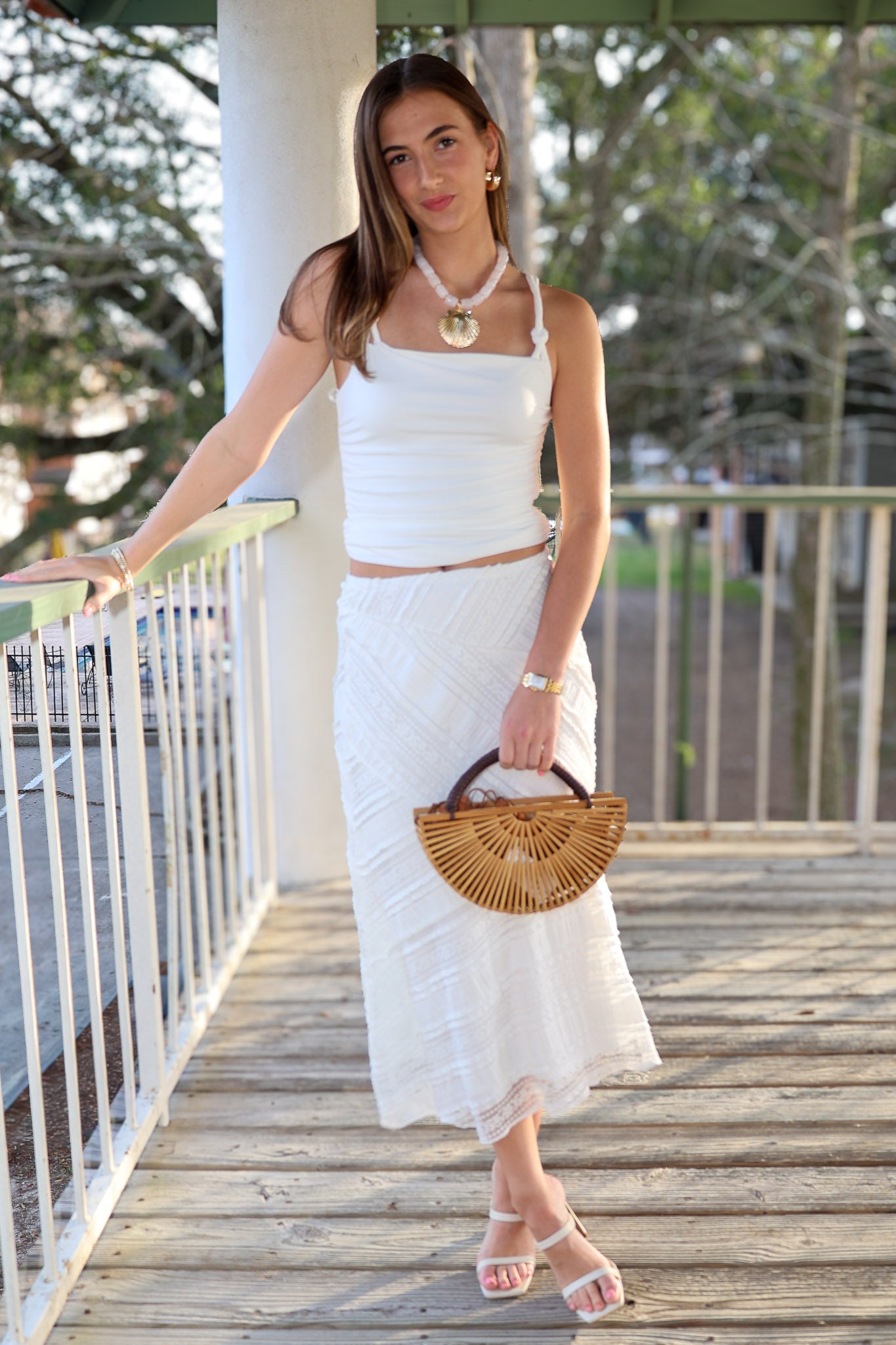 Woman in a white outfit holding a wooden handbag on a wooden deck on vacation