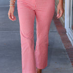A person wearing red and white gingham cropped pants and a matching red and white gingham top, walking outdoors on a sidewalk.