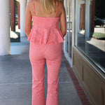 A woman viewed from behind wearing a red and white gingham two-piece set consisting of a spaghetti-strap peplum top and matching cropped pants, walking on a covered outdoor walkway.