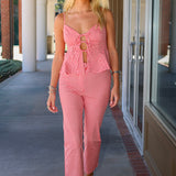 A woman modeling a red and white gingham two-piece set consisting of a sleeveless top with keyhole cutouts and matching cropped pants, walking on an outdoor covered walkway.
