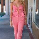 A woman modeling a red and white gingham two-piece set consisting of a sleeveless crop top with a keyhole cutout and matching cropped straight-leg pants, walking on an outdoor walkway.