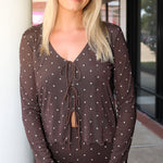 A smiling blonde woman wearing the Amara brown long-sleeve V-neck top with white polka dots by Z Supply and a tie-front detail, paired with a matching brown Eda polka-dot skirt at Rodeo Boutique.
