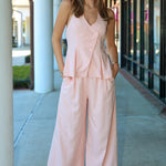 Woman wearing a pink matching vest and pant suit standing outdoors on a sidewalk.