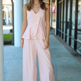Woman wearing a light pink outfit standing on a sidewalk.