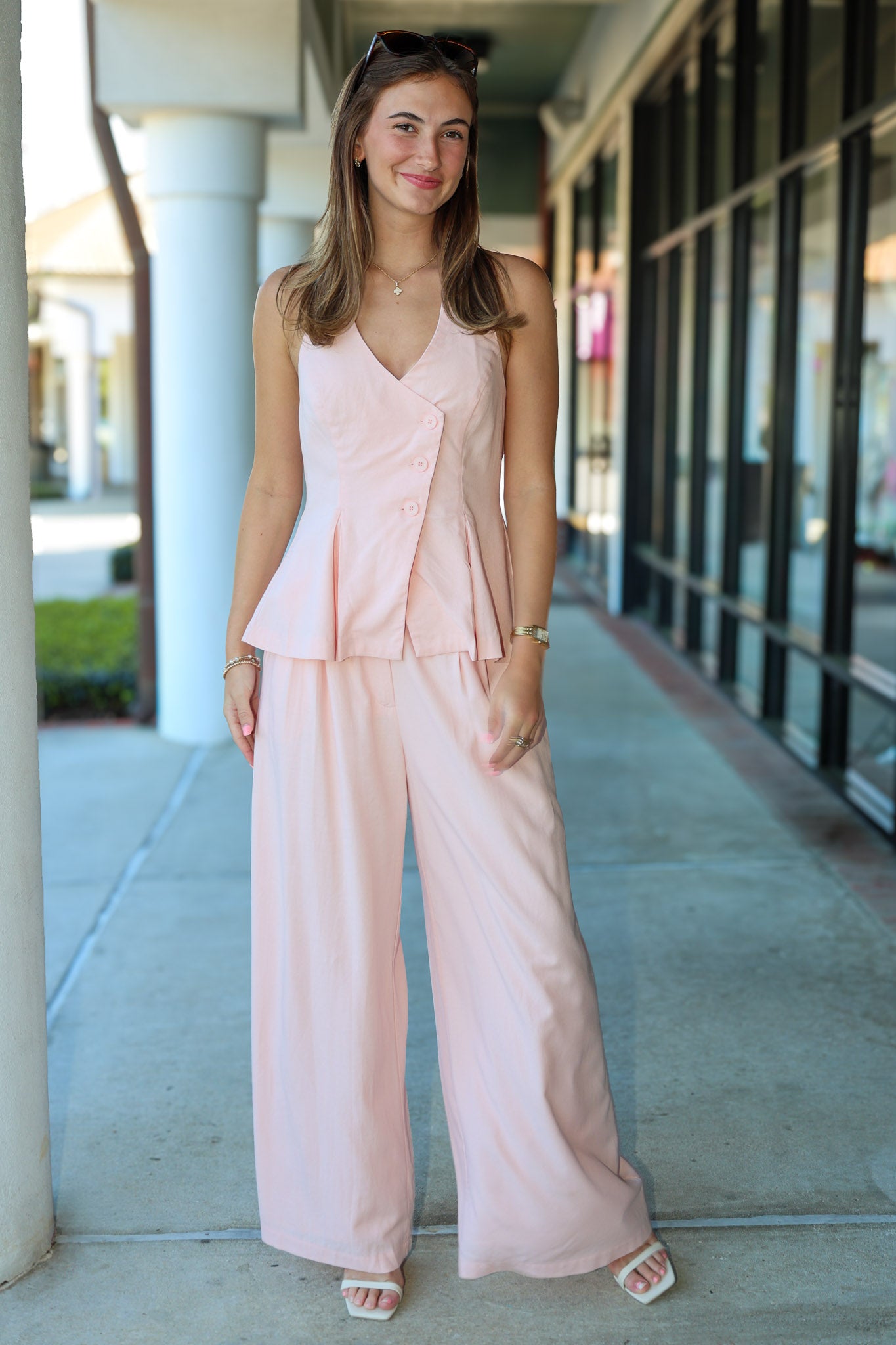 Woman wearing a light pink outfit standing on a sidewalk.