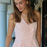 Woman wearing a light pink vest with sunglasses on her head, standing outdoors.