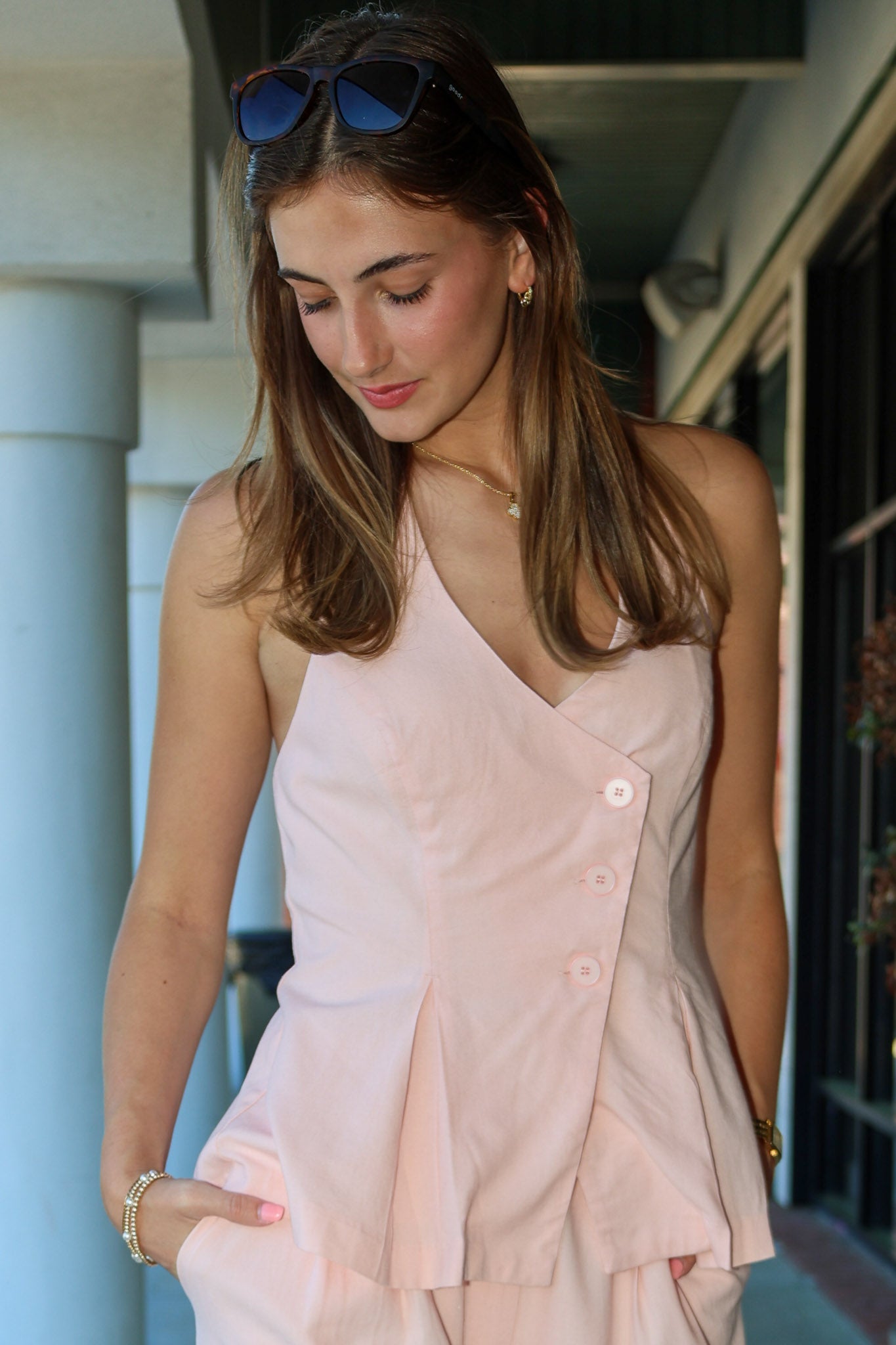Woman wearing a light pink vest with sunglasses on her head, standing outdoors.