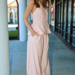 Woman wearing a pink matching vest and pant suit standing outdoors on a sidewalk.