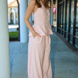 Woman wearing a pink matching vest and pant suit standing outdoors on a sidewalk.