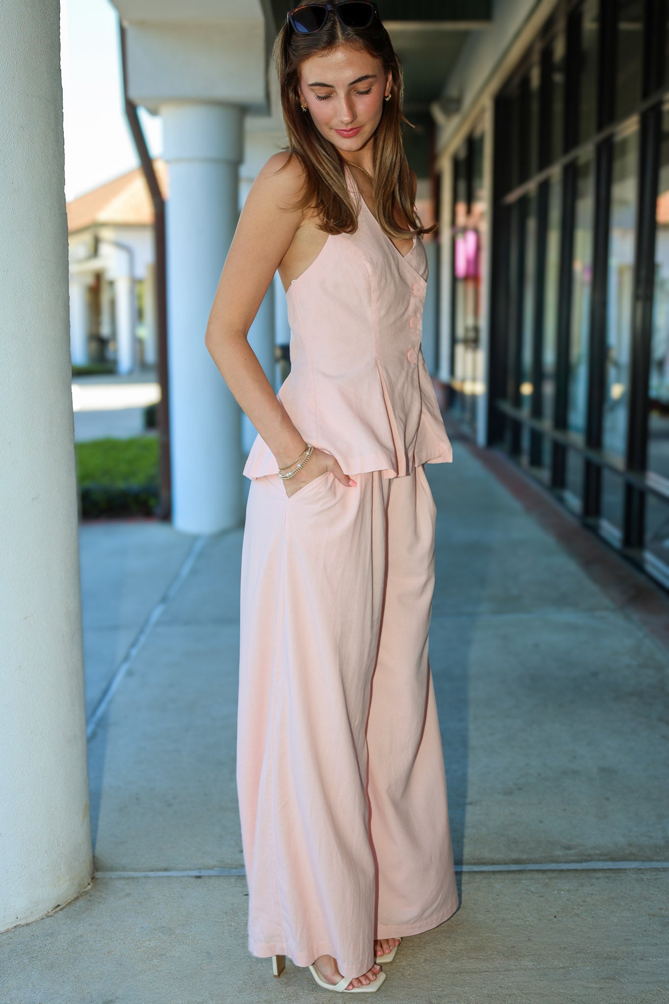 Woman wearing a pink matching vest and pant suit standing outdoors on a sidewalk.