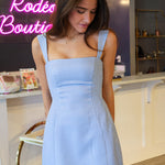 Woman wearing a blue checkered dress in a store setting with neon signs.