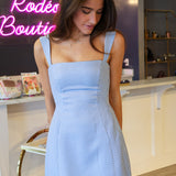 Woman wearing a blue checkered dress in a store setting with neon signs.