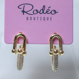 A pair of gold-tone drop earrings with pavé crystal chains, displayed on a pink card labeled 'Rodéo BOUTIQUE'.