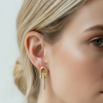 A close-up of a woman's ear wearing a gold hoop earring with a dangling chain of small clear stones, shown against her blonde hair and face.