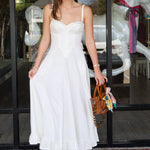 Woman in a white dress standing outside a store with glass doors.