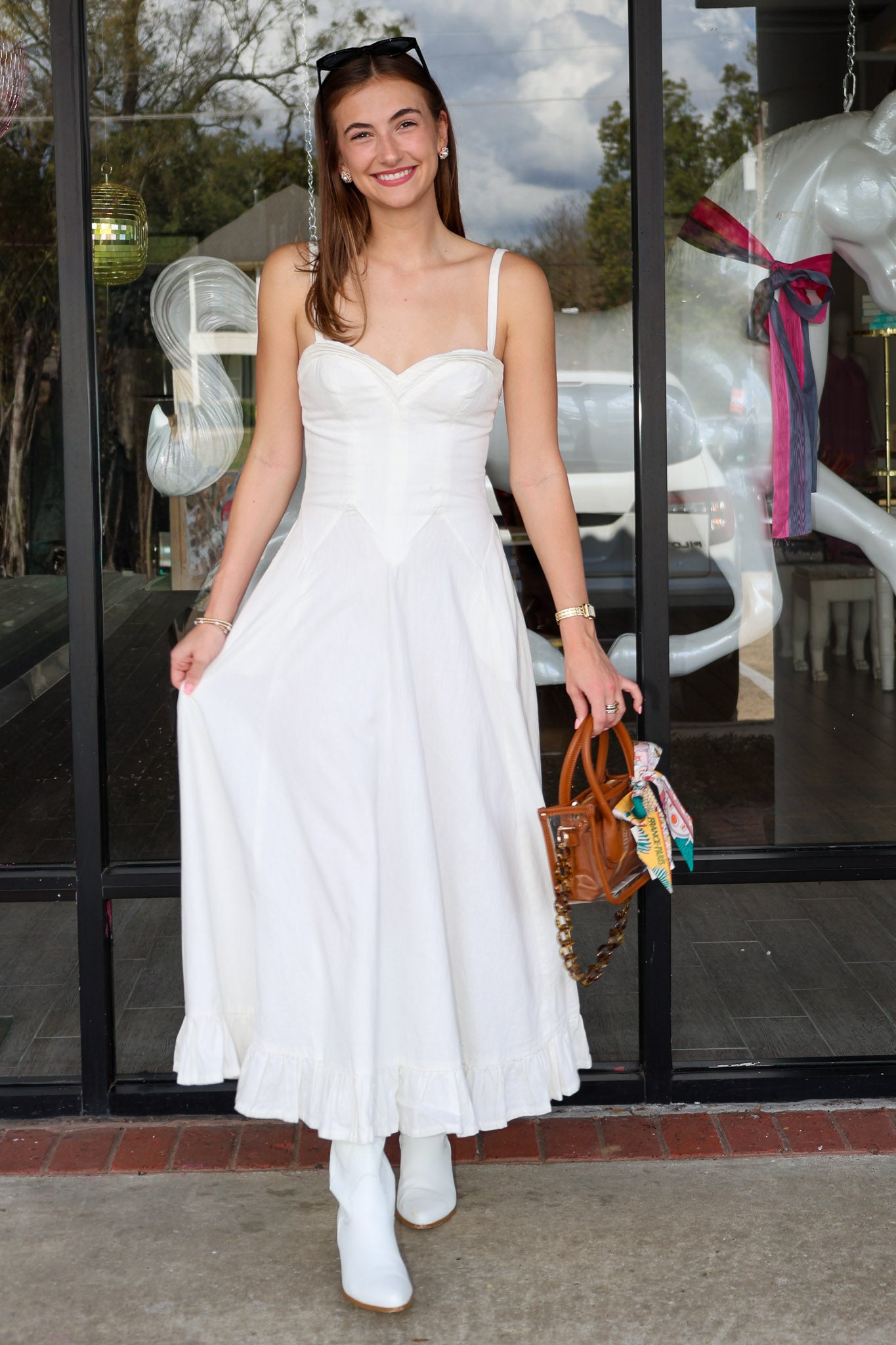 Woman in a white dress standing outside a store with glass doors.