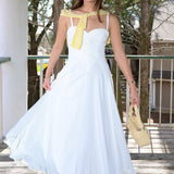 Woman in a white dress with a yellow scarf and handbag standing on a wooden deck.