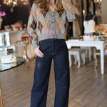 Woman wearing a patterned argyle cardigan and dark jeans in an indoor setting