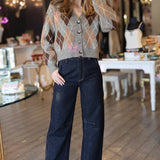 Woman wearing a patterned argyle cardigan and dark jeans in an indoor setting