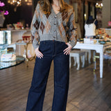 Woman in a patterned argyle cardigan and dark jeans standing in an indoor setting with tables and chairs.