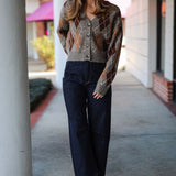 Woman wearing a patterned argyle  cardigan and dark jeans standing on a sidewalk.