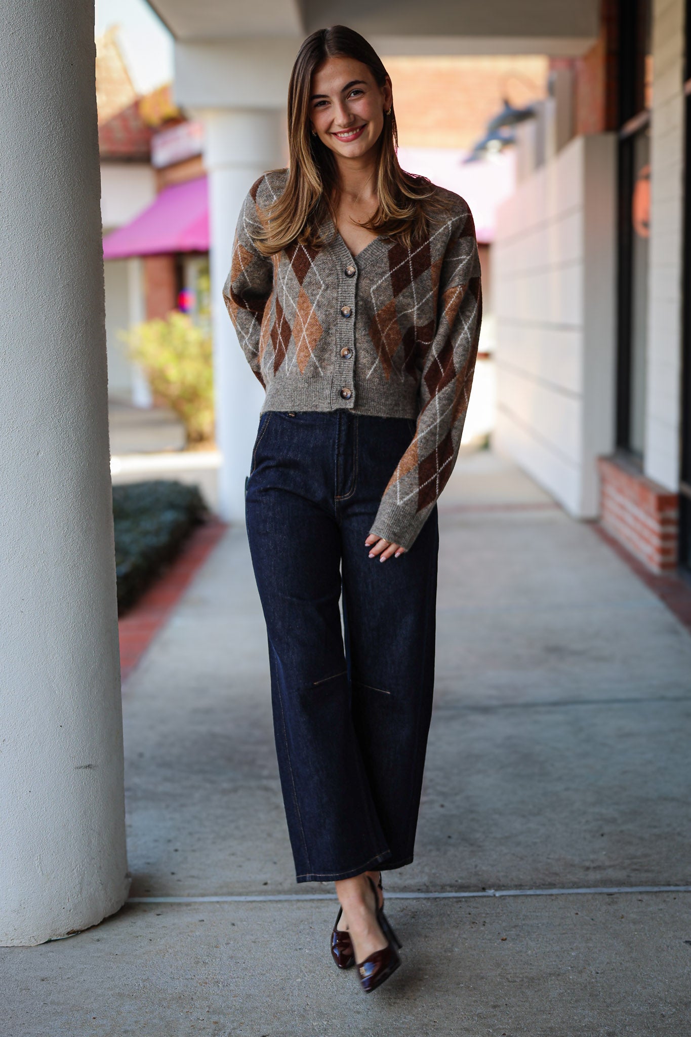 Woman wearing a patterned argyle  cardigan and dark jeans standing on a sidewalk.