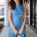 Woman wearing a blue denim dress holding a transparent handbag with a colorful interior.