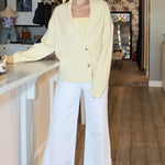Woman in a yellow cardigan and white pants standing in a kitchen.
