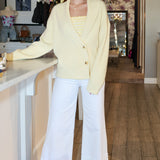 Woman in a yellow cardigan and white pants standing in a kitchen.