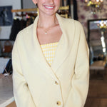 Woman wearing a light yellow cardigan over a patterned top in an indoor setting.