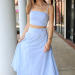 Woman wearing a light blue stripe two-piece outfit standing outdoors.