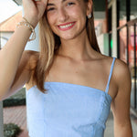 Woman wearing a light blue and white stripe top with thin straps outdoors.