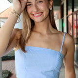 Woman wearing a light blue and white stripe top with thin straps outdoors.
