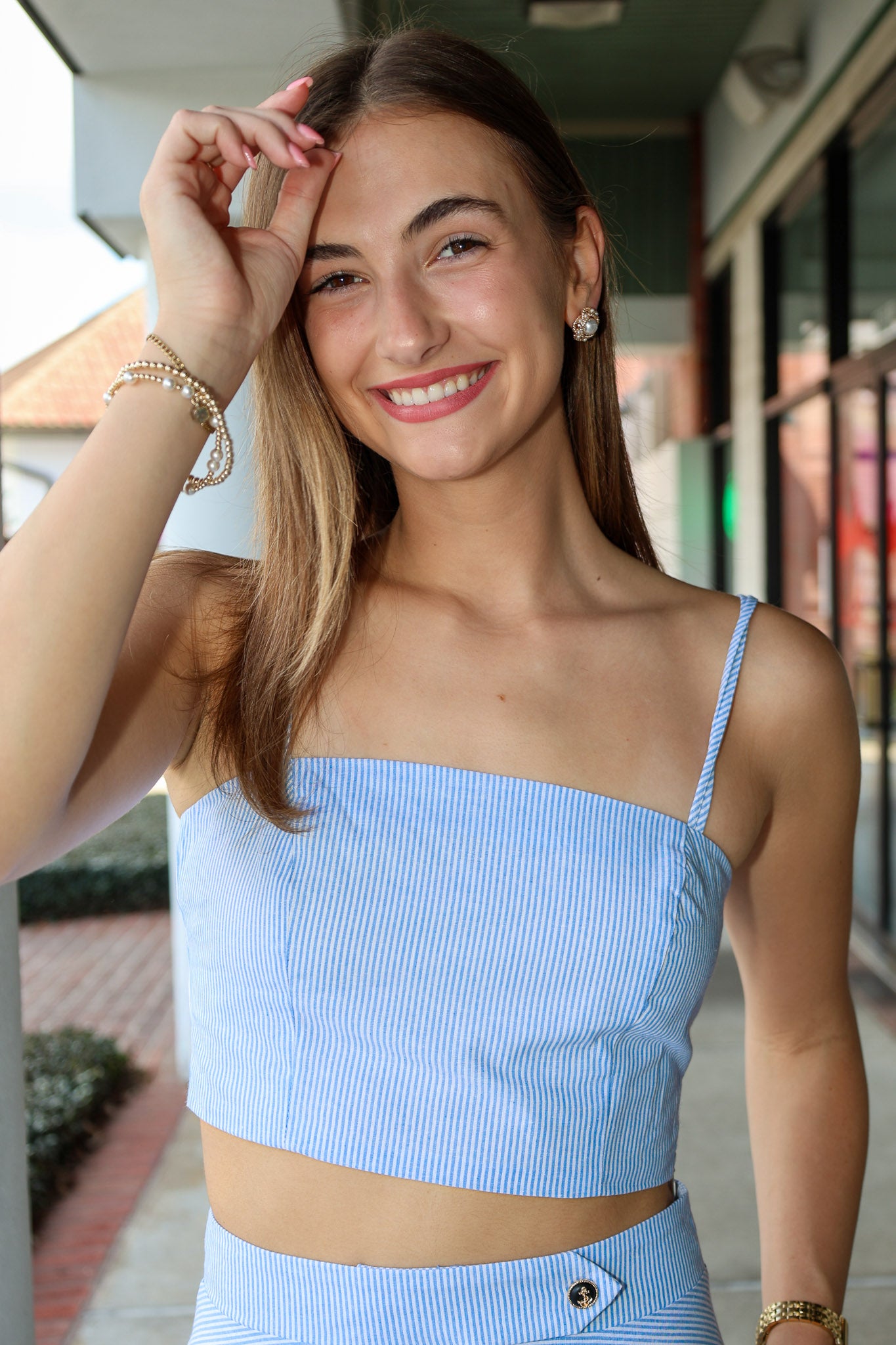 Woman wearing a light blue and white stripe top with thin straps outdoors.