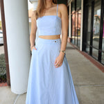 Woman wearing a light blue stripe outfit standing on a sidewalk.