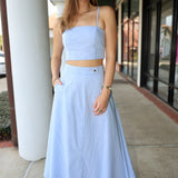 Woman wearing a light blue stripe outfit standing on a sidewalk.