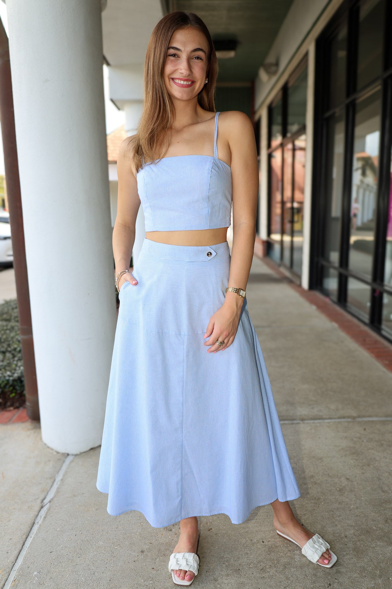 Woman wearing a light blue stripe outfit standing on a sidewalk.