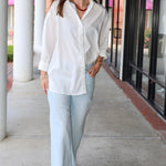 Bea Shirt, NIA - white button down shirt and light blue PISTOLA jeans standing on a sidewalk.